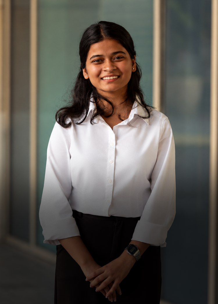 A young woman stands in front of an office building, smiling.